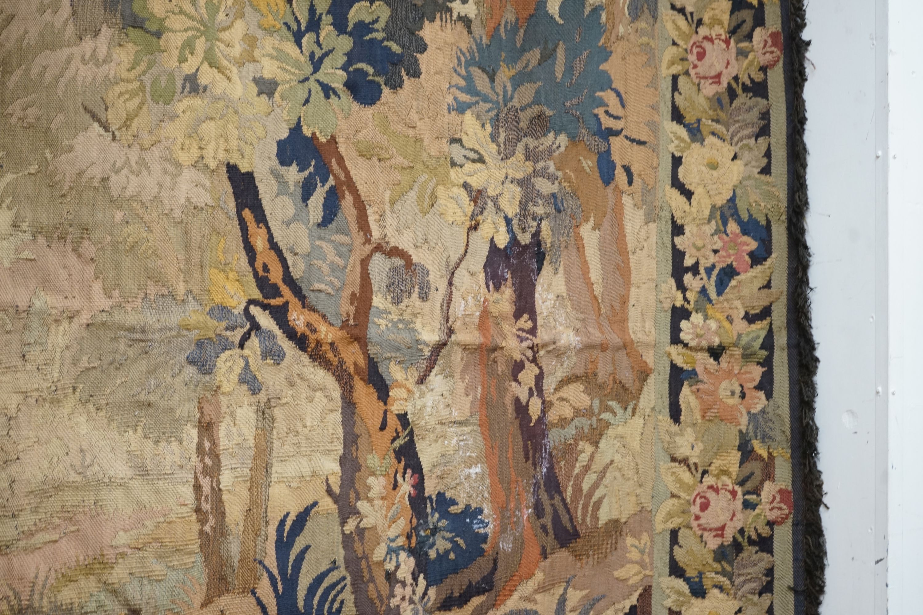 A late 19th / early 20th century French tapestry depicting a woodland scene with trees and flowers with a floral border woven in autumnal colours